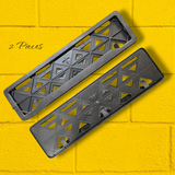 Two gray metal brackets with geometric design on a yellow brick wall background